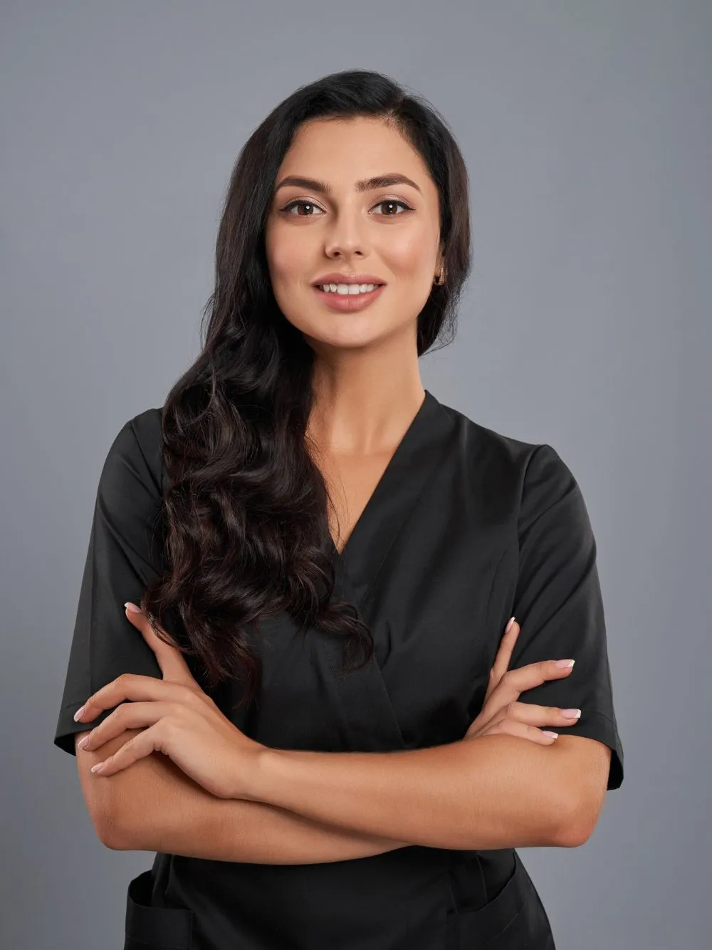 attractive-female-beautician-black-uniform-standing-with-crossed-arms-grey-background-edited